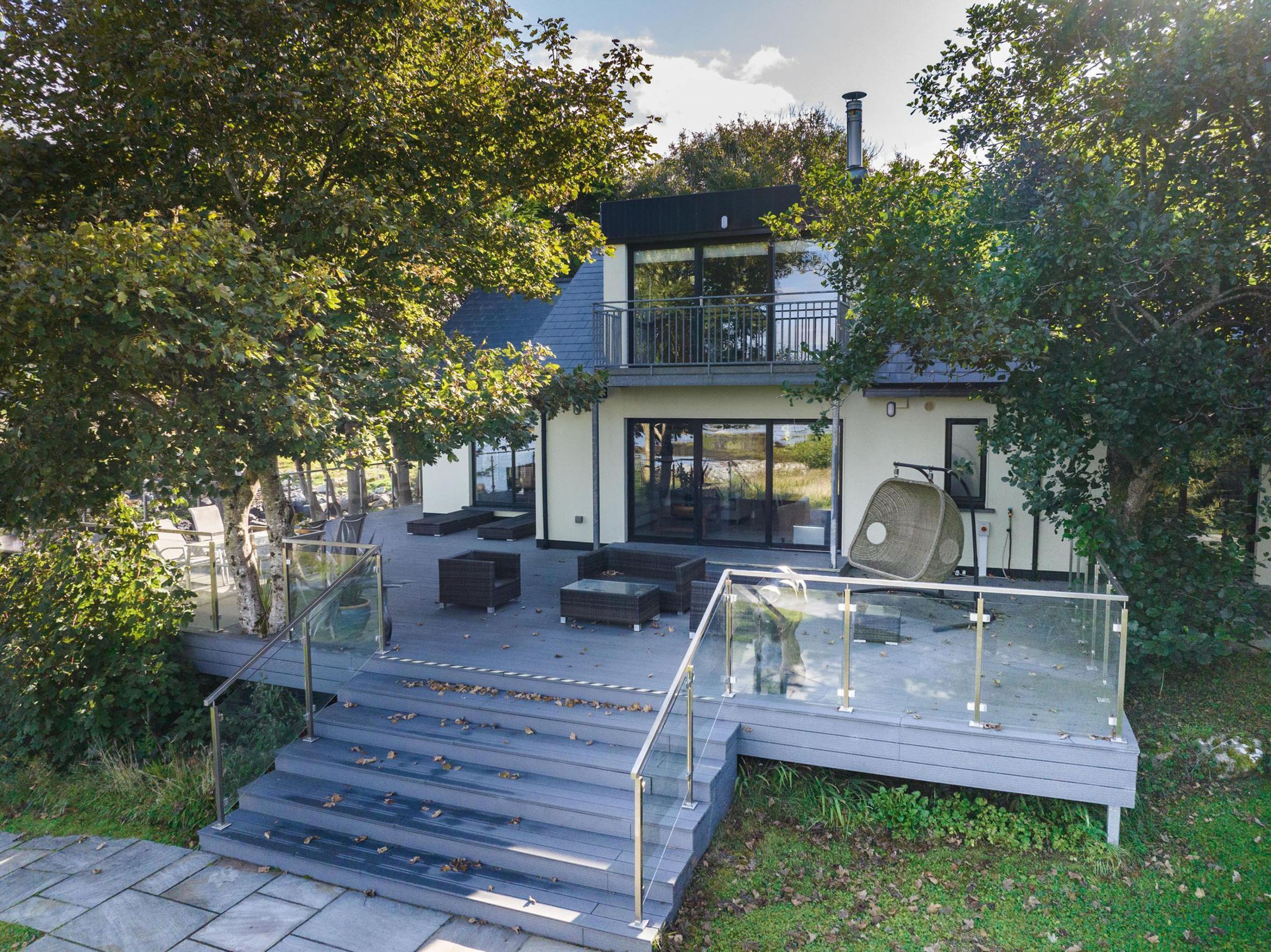 A modern two-story house with a glass-enclosed deck and outdoor seating area.