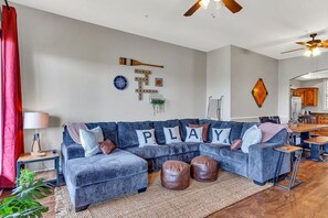 A living room with a blue sofa, leather ottomans, a coffee table, a red curtain, a lamp, and a wall with decorative items including a 'PLAY' sign.