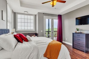 Une chambre à coucher avec un lit, un ventilateur de plafond, une télévision, une commode et une porte-fenêtre donnant sur un balcon.