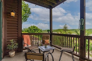 A covered outdoor seating area with a table and chairs, a potted plant, and a view of the landscape.