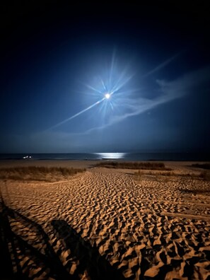A nighttime beach scene with a bright moon or sun in the sky, sandy beach, and a distant shoreline. - Beautiful Beach front home- 150 yards to the white sand beach (Biloxi)