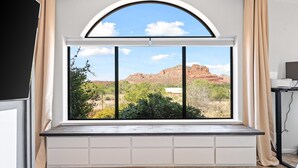 Quarto com uma grande janela arqueada com vista para uma paisagem desértica com formações rochosas avermelhadas e vegetação rasteira.