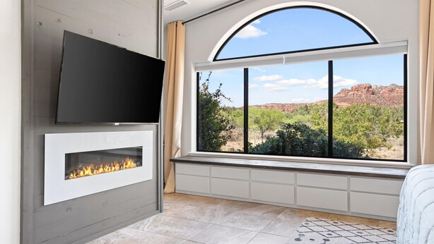 Quarto moderno com lareira, uma janela grande com vista para formações rochosas avermelhadas e uma TV de tela plana fixada na parede.