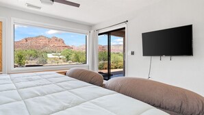 Quarto com uma cama grande, uma TV fixada na parede e uma janela com vista para formações rochosas avermelhadas.