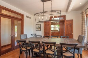 A dining area with a large wooden table, six chairs, and a hanging light fixture.