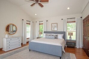 A bedroom with a bed, dresser, ceiling fan, and windows with curtains.
