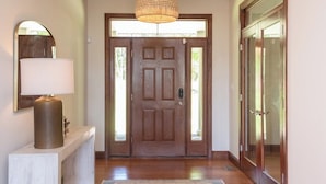 Una puerta de madera con un panel de vidrio, una lámpara colgante y una consola blanca con una lámpara.