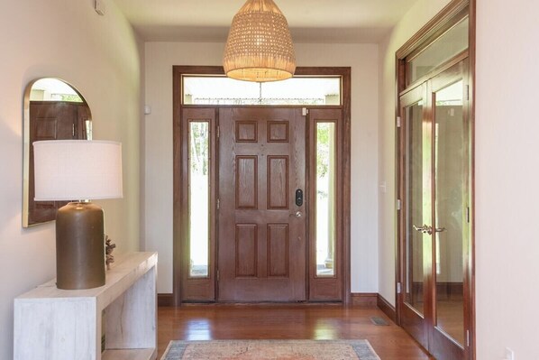 Una puerta de madera con un panel de vidrio, una lámpara colgante y una consola blanca con una lámpara.