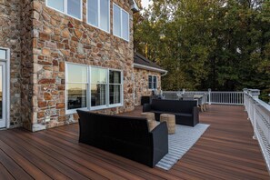 A stone exterior wall, a deck with wooden flooring, outdoor furniture, and a white railing.