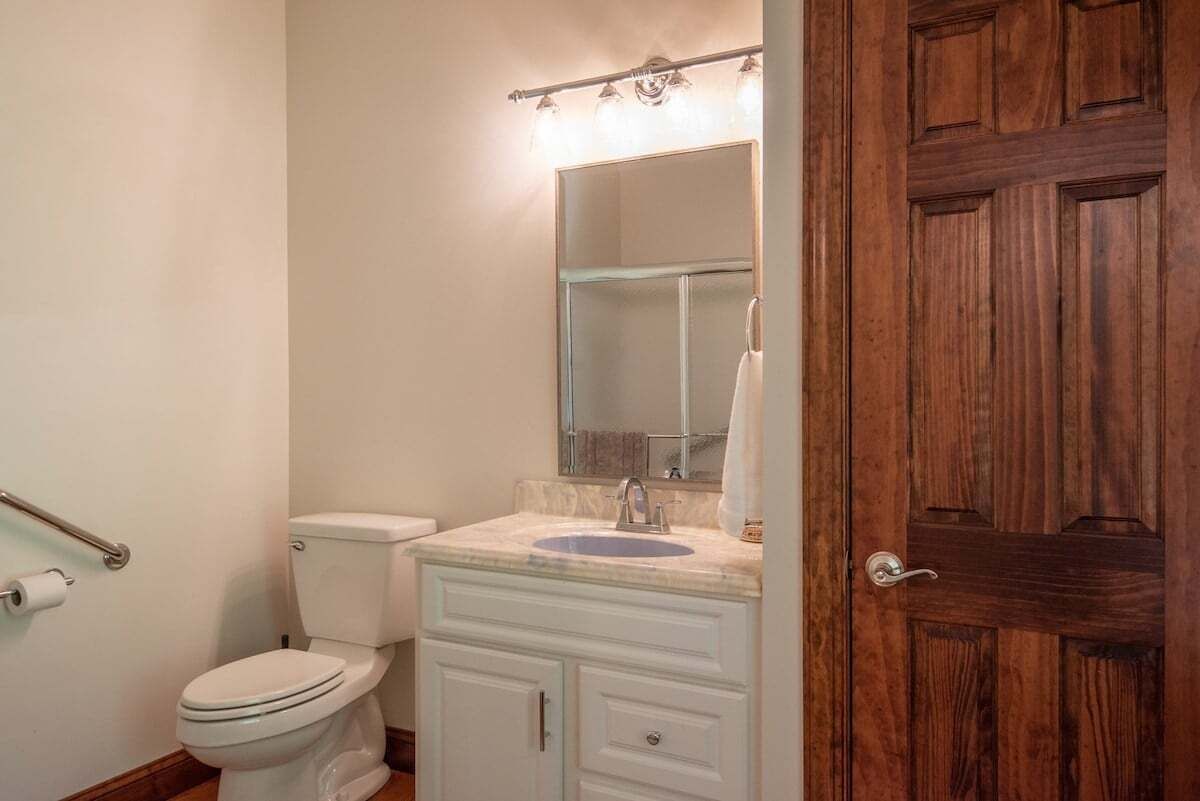 Un baño con inodoro, lavabo, espejo y puerta de madera.