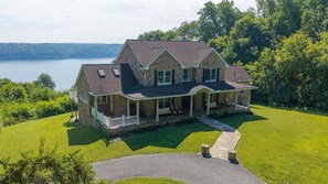 A two-story stone house with a wrap-around porch, a stone pathway leading to the entrance, and a view of a lake. - Waterfront Retreat w/ Hot Tub, Games & Views (Whiteford)