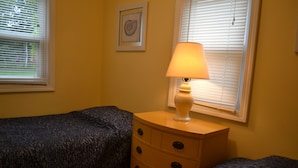 Una camera da letto con due letti, un comodino con una lampada, un quadro appeso al muro e una finestra con persiane.