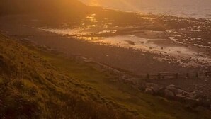 A coastal landscape with a sunset over the ocean, a rocky shoreline, and grassy hills. - A beautiful, unique lodge, made for two (Lampeter)
