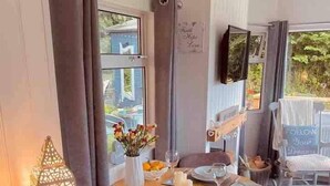 A dining area with a round table set for four, a vase of flowers, and a lit lantern. - A beautiful, unique lodge, made for two (Lampeter)