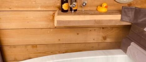 A wooden cabin interior with a hot tub, two champagne bottles, glasses, and a rubber duck. A sign reads "Happy Retirement."