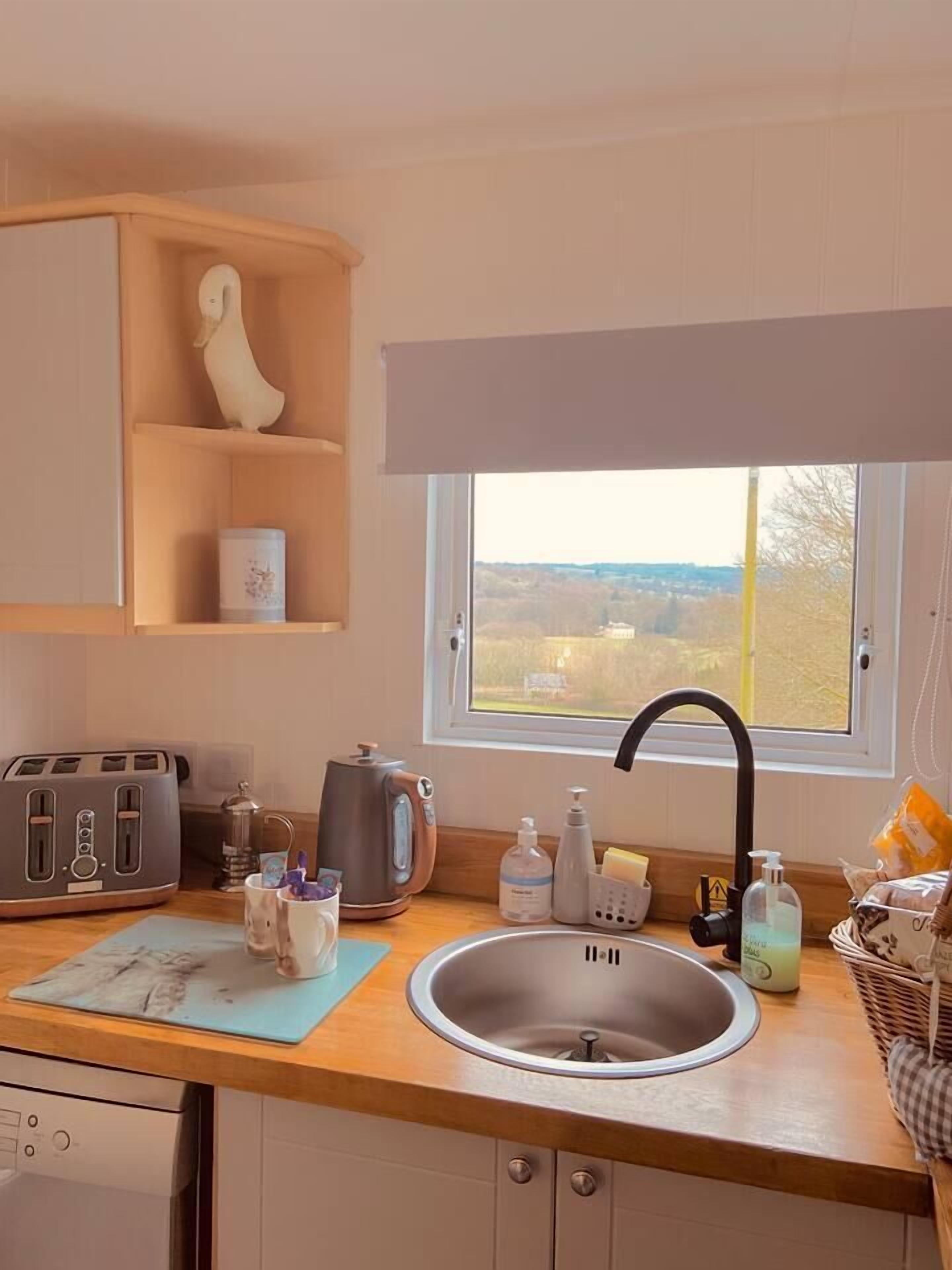 Una cucina con una finestra, un tostapane, un bollitore, un lavandino e uno scaffale in legno con un oggetto decorativo.