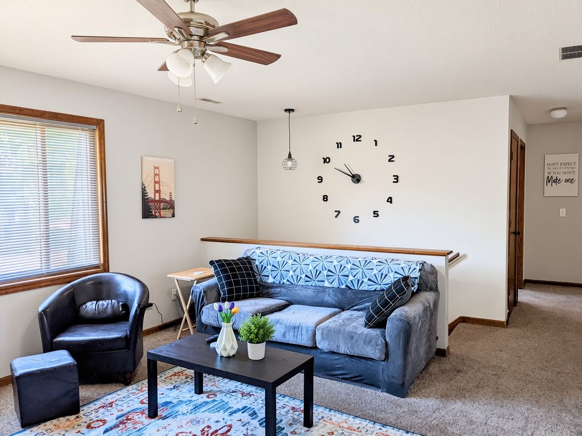 Una sala de estar con sofá, sillón, mesa de centro y un reloj de pared.