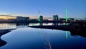 A bridge with green lights reflecting on the water.