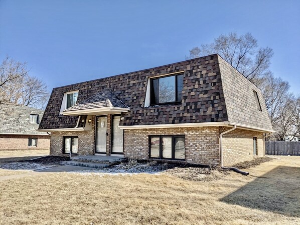 A modern two-story house with a brick exterior and a sloped roof. - Renovated 2BR Retreat • Minutes from Downtown Omaha (Council Bluffs)