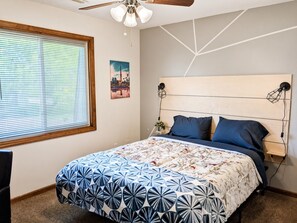 Ein Schlafzimmer mit einem Bett, einem Fenster mit Jalousien, einem Deckenventilator und einer Wandlampe.