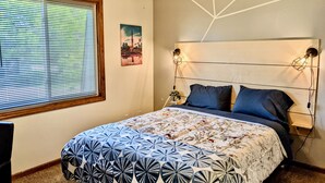 A bedroom with a bed, a ceiling fan, a wall-mounted light, and a window with blinds.
