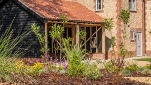 Una casa con fachada de ladrillo, un porche de madera y un jardín con diversas plantas y flores.