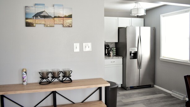 Una cocina moderna con refrigerador de acero inoxidable, gabinetes blancos y una mesa de madera con cafetera.
