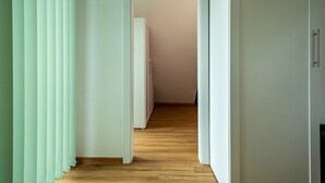 A hallway with wooden flooring, white walls, and a door leading to another room. - Alpenblick Apartment with Mountain View, Balcony, and Wi-Fi (Friedrichshafen)
