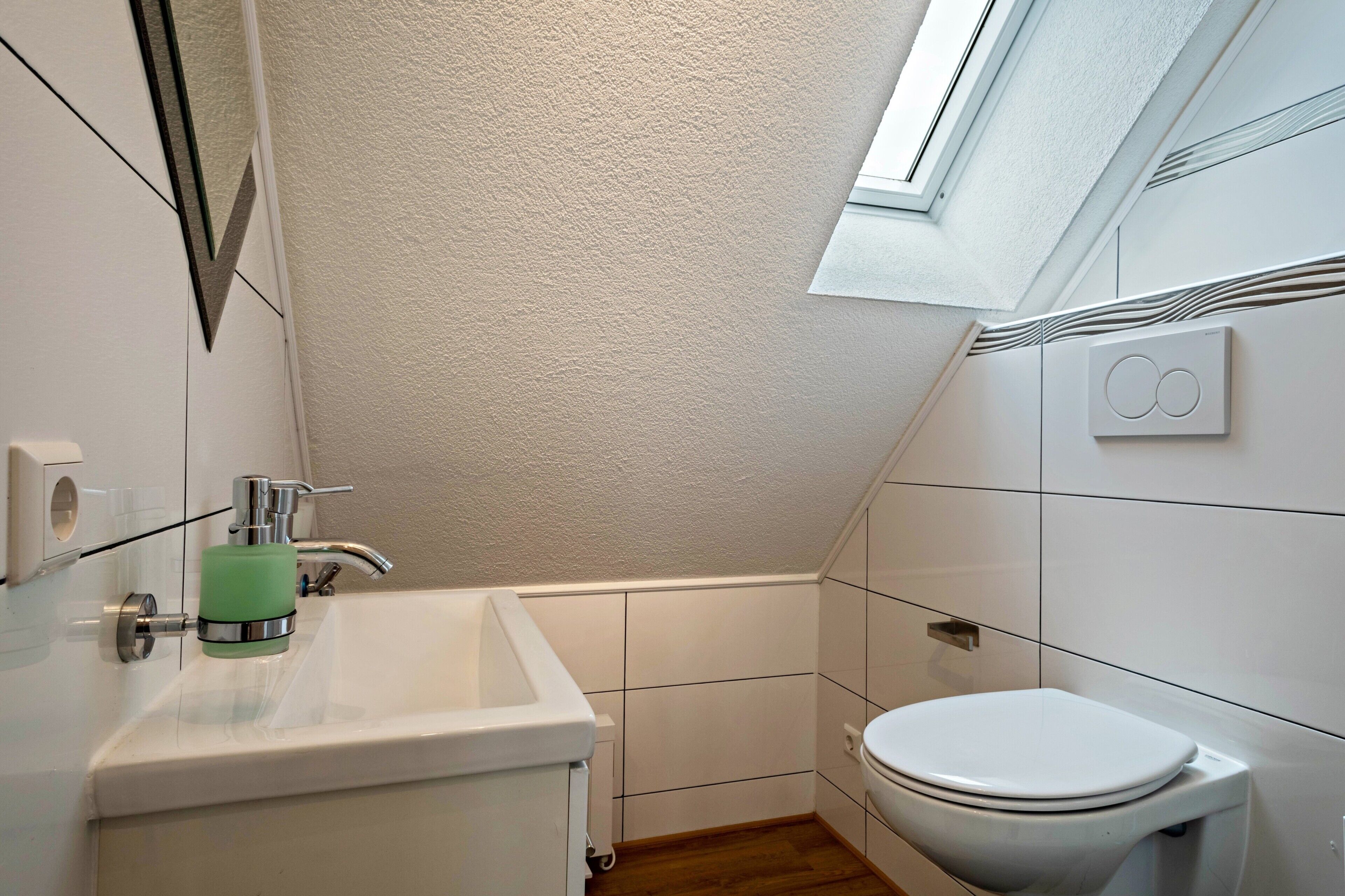 A small bathroom with a white sink, a toilet, and a skylight.