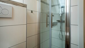A modern bathroom with a glass shower enclosure, white tiled walls, and a visible water heater. - Alpenblick Apartment with Mountain View, Balcony, and Wi-Fi (Friedrichshafen)