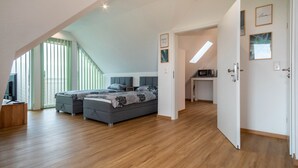 A modern bedroom with a loft-style ceiling, a bed with grey bedding, a desk with a computer, and a view of the outdoors. - Alpenblick Apartment with Mountain View, Balcony, and Wi-Fi (Friedrichshafen)