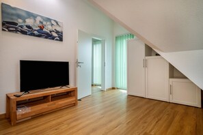 Un salon moderne avec un téléviseur à écran plat posé sur un meuble en bois, un tableau accroché au mur et un escalier menant à l’étage supérieur.