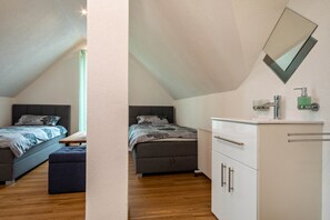 Une chambre avec deux lits, une commode blanche, un miroir et une fenêtre.