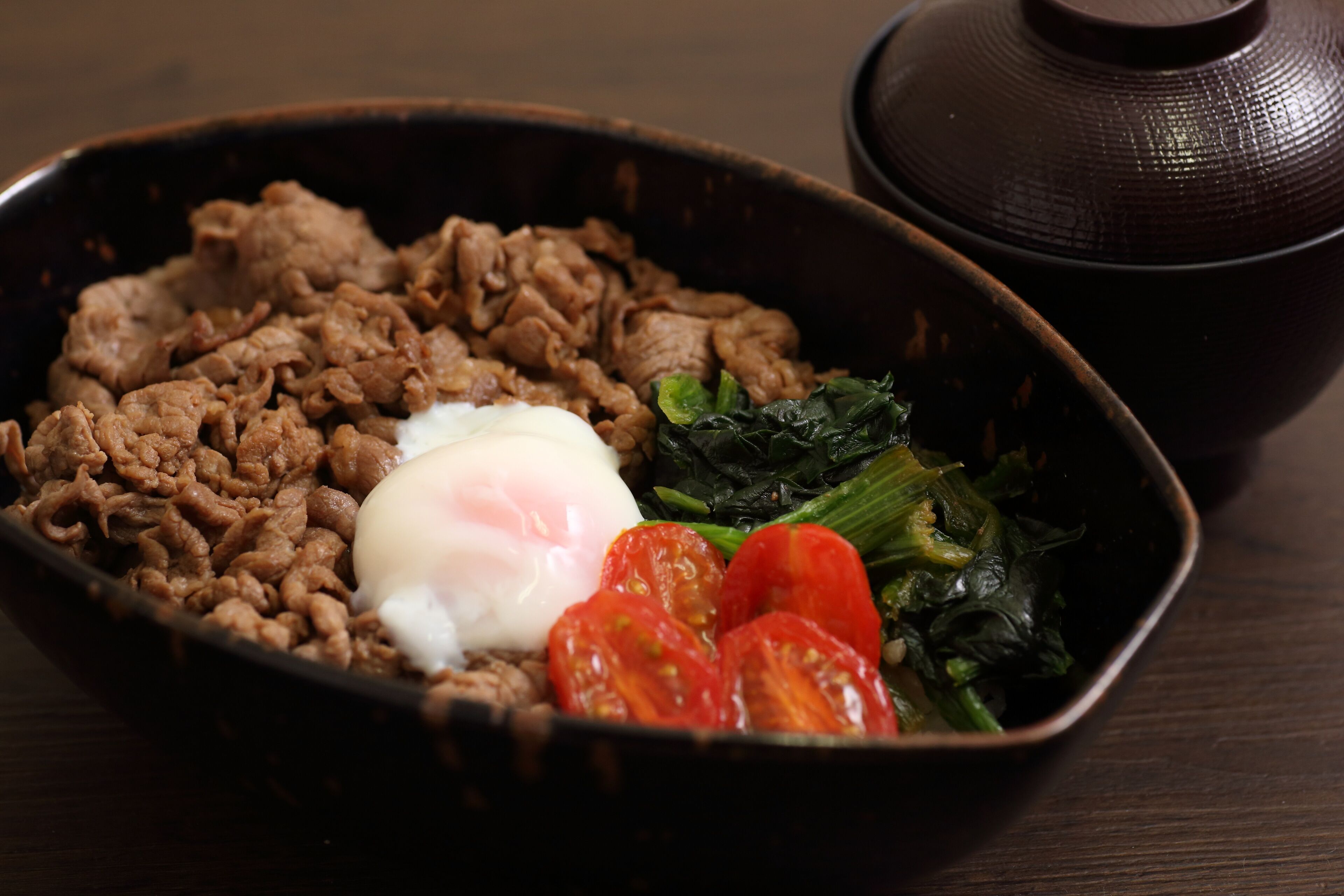 Un plato de comida con carne, un huevo escalfado, tomates y verduras de hoja verde.
