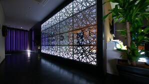 A hallway with a decorative wall featuring geometric patterns, a potted plant, and a reception area with a counter and items on it. - Hotel LUNE CLAIRE - Adults Only (Chikuma)