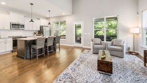 A spacious kitchen with white cabinets, a central island with bar stools, and a large window providing a view of greenery. - Peaceful Lake Home on TIms Ford (Tullahoma)