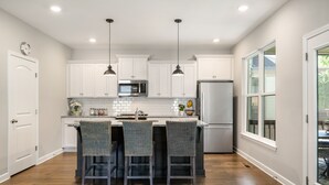 A modern kitchen with white cabinets, a central island with bar stools, stainless steel appliances, pendant lighting, and a large window providing natural light. - Peaceful Lake Home on TIms Ford (Tullahoma)