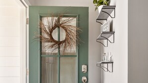 A teal door with a wreath, a doormat, and a wall-mounted shelf with books and a plant. - Peaceful Lake Home on TIms Ford (Tullahoma)