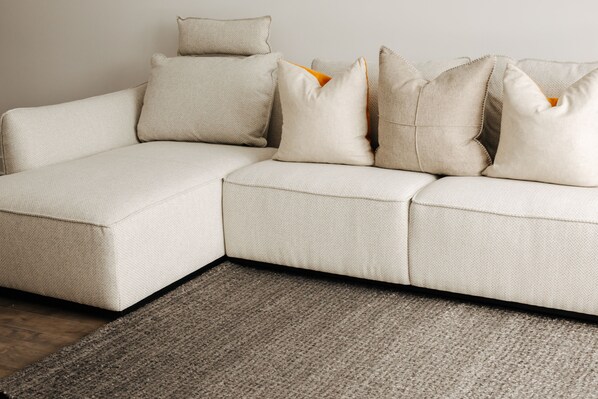 A sectional sofa with multiple cushions and a textured rug on a wooden floor.