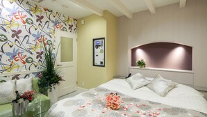 Une chambre d’hôtel avec un lit, une table en verre sur laquelle se trouvent une bouteille et des fleurs, un mur orné d’un motif floral et un tableau encadré accroché au mur.