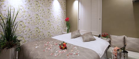 A neatly arranged bedroom with a large bed, a bedside table with a glass top, and a potted plant.