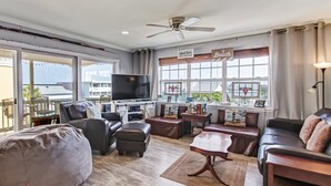 A spacious living room with a large flat-screen TV, leather sofas, a coffee table, and a bean bag. - Tybee South Beach Condo, Heated Pool Access (Tybee Island)