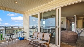 A covered outdoor area with a seating arrangement, a table, and a view of the surrounding buildings. - Tybee South Beach Condo, Heated Pool Access (Tybee Island)