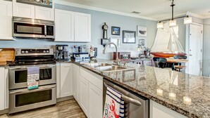 A kitchen with white cabinets, stainless steel appliances, a granite countertop, and a sailboat decoration. - Tybee South Beach Condo, Heated Pool Access (Tybee Island)