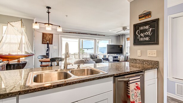 A modern kitchen with granite countertops, stainless steel appliances, and a large window offering a view of the outdoors. - Tybee South Beach Condo, Heated Pool Access (Tybee Island)
