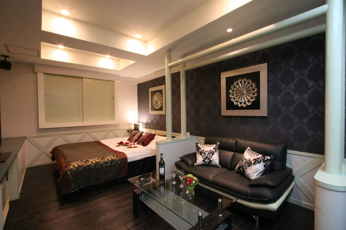 Una habitación de hotel moderna con una cama grande, un sofá de cuero, una mesa de centro de vidrio y arte decorativo en la pared.