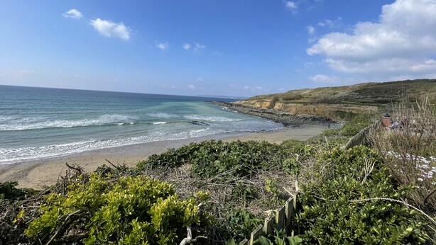 Un paisaje costero con playa, acantilados rocosos y vegetación.