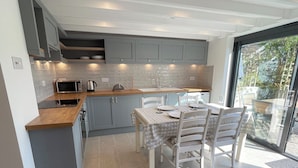Una cocina moderna con armarios grises, encimera de madera y zona de comedor con una mesa dispuesta para cuatro.