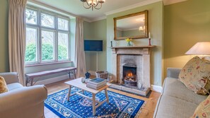 Cozy living room with a fireplace, sofa, and bench by the window, featuring a flat-screen TV and a decorative mirror above the fireplace.