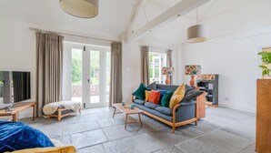 A spacious living room with a grey sofa, a wooden coffee table, and a TV on a stand.